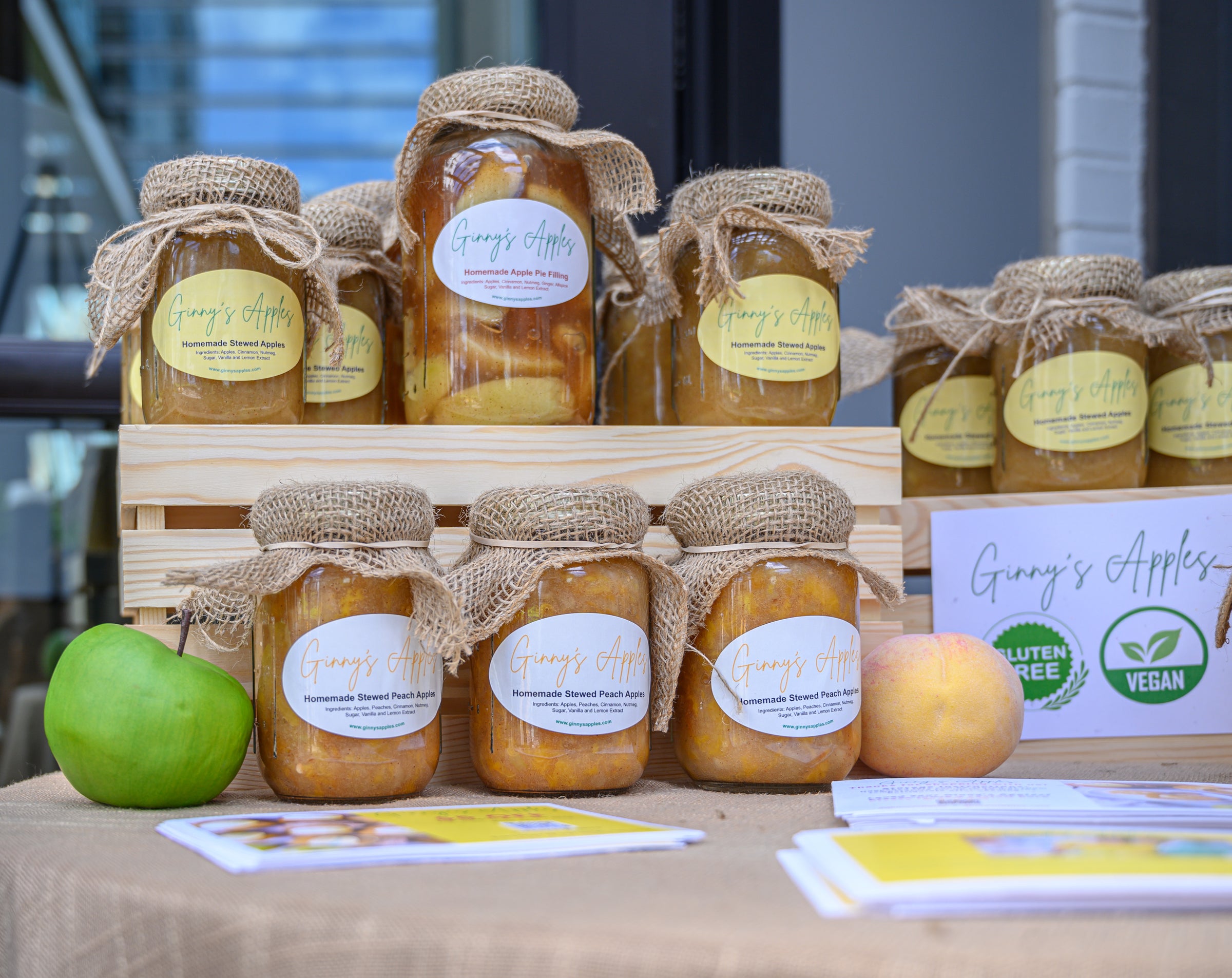 Jars of Ginny's Apples with burlap tops on a market table, a green apple beside them